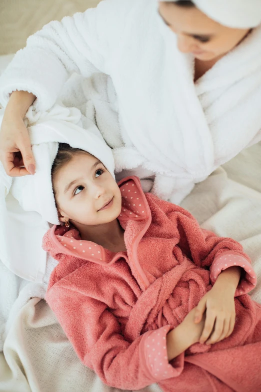 a woman laying on top of a bed next to a little girl, pexels contest winner, bathrobe, wearing a towel, thumbnail, closeup - view