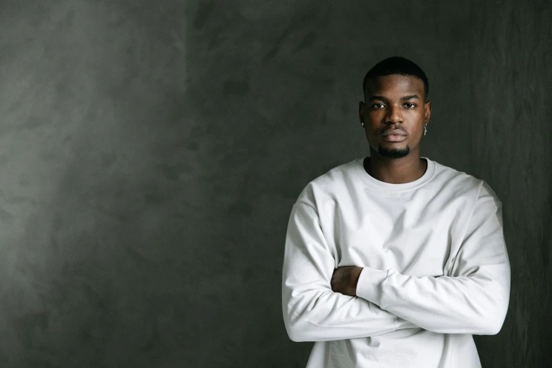 a man in a white shirt standing with his arms crossed, an album cover, inspired by Paul Georges, pexels contest winner, wearing a dark sweater, ( ( dark skin ) ), he is about 20 years old, promotional image