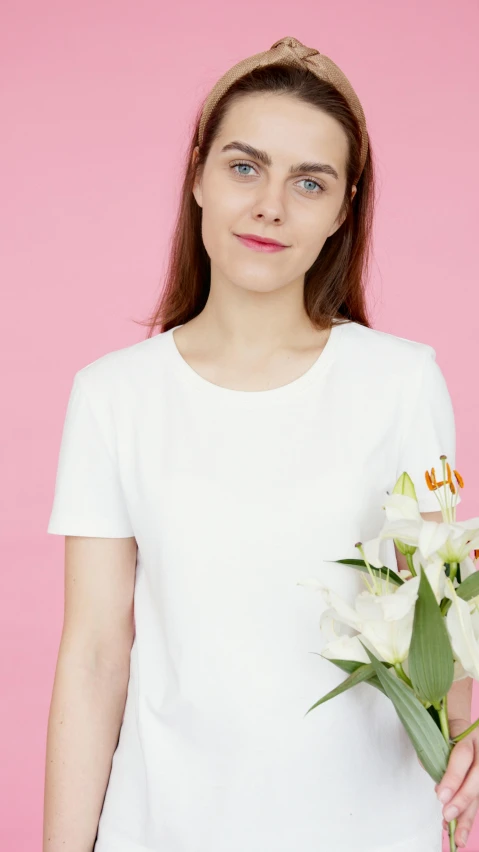 a woman holding a bouquet of flowers against a pink background, inspired by Andrée Ruellan, shutterstock contest winner, minimalism, white t-shirt, low quality photo