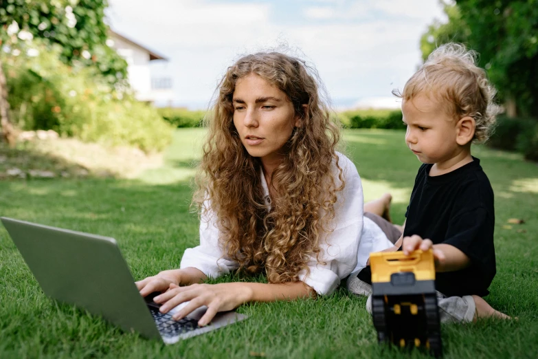 a woman and a child laying on the grass with a laptop, by Carey Morris, pexels contest winner, robotics, avatar image, people at work, handheld