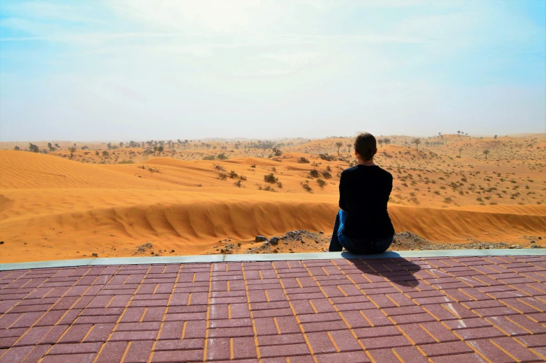 a person sitting on top of a roof in the desert, by Julia Pishtar, pexels contest winner, sandy colours, dune, vista view, ameera al taweel