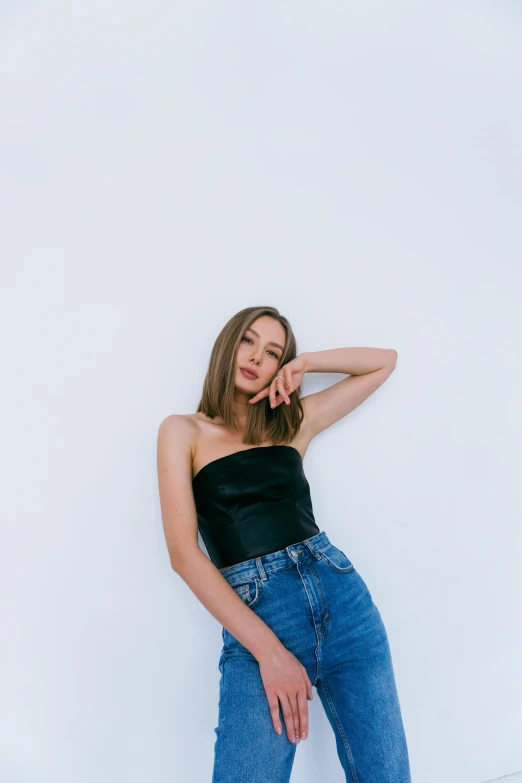 a woman in a black top and jeans leaning against a white wall, an album cover, trending on pexels, portrait sophie mudd, nft portrait, croptop, ekaterina