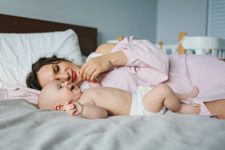 a woman laying on top of a bed next to a baby, pexels contest winner, manuka, thumbnail, 1 2 9 7