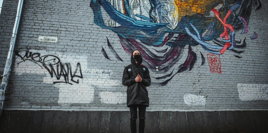 a man standing in front of a graffiti covered wall, pexels contest winner, wearing black hooded cloak, instagram post, full body picture, balaclava covering face