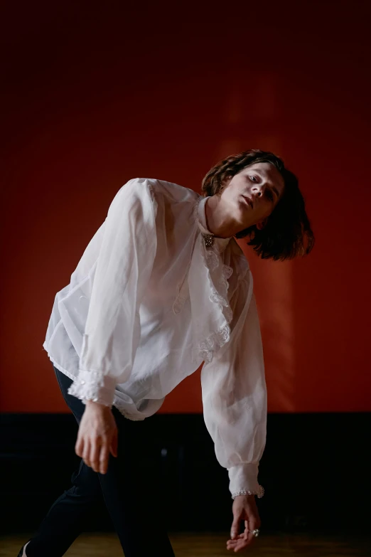 a woman in white shirt doing a trick on a skateboard, an album cover, unsplash, bauhaus, portrait of timothee chalamet, standing in a dimly lit room, loose - fitting blouses, against a red curtain