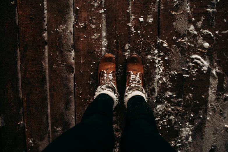 a person standing on a wooden floor covered in snow, inspired by Elsa Bleda, trending on pexels, brown boots, looking up at the camera, texturized, background image
