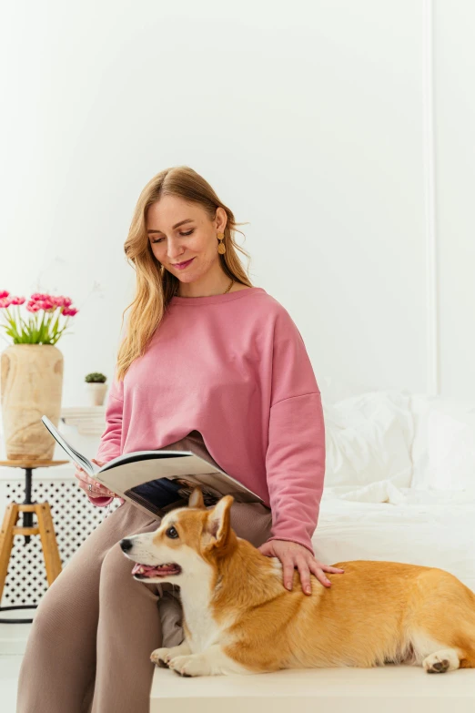 a woman sitting on a bed reading a book with her dog, by Grytė Pintukaitė, happening, wearing a pastel pink hoodie, smart casual, bench, ergonomic