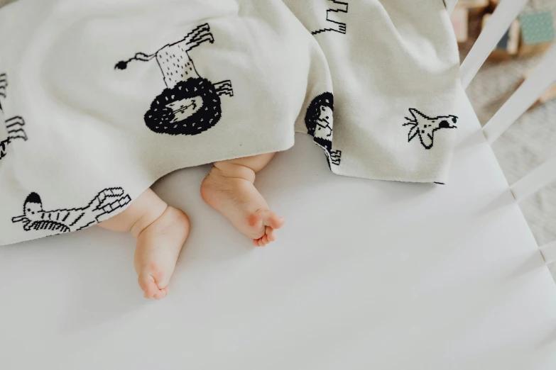 a close up of a baby laying in a crib, a child's drawing, trending on pexels, lying in bed!!!! blanket, three animals, printed on a cream linen t-shirt, detailed legs