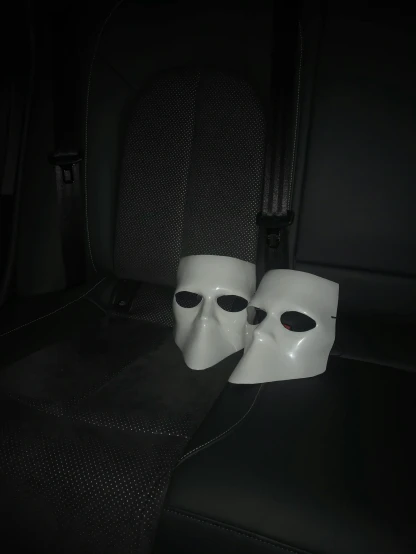 two white masks sitting in the back of a car, by Thomas Furlong, reddit, discord profile picture, dark. no text, put on a mannequin, low quality photo