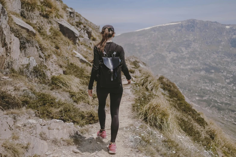 a woman hiking up the side of a mountain, pexels contest winner, figuration libre, wearing fitness gear, walking away from the camera, black, spanish