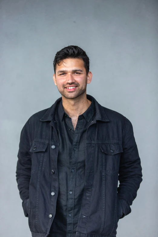 a man standing in front of a gray wall, wearing a black shirt, ash thorp khyzyl saleem, on clear background, giddy smirk