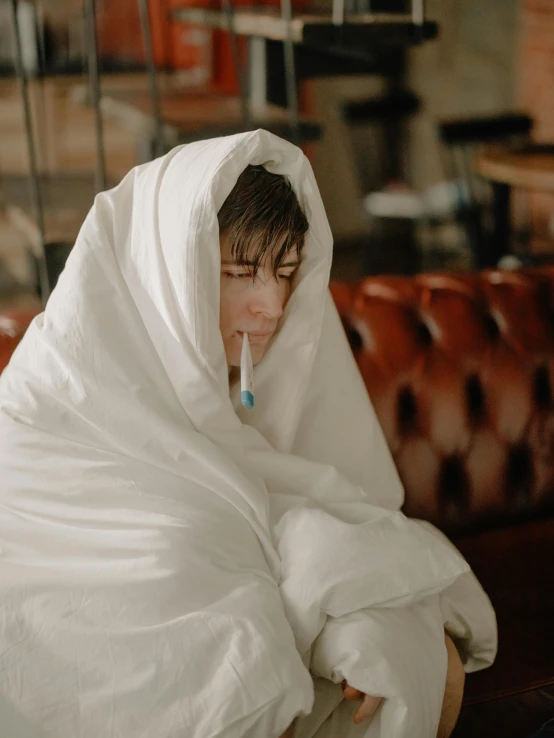 a woman sitting on a couch wrapped in a blanket, inspired by Elsa Bleda, unsplash contest winner, happening, cigarette in his mouth, wearing white silk hood, sitting in a cafe alone, declan mckenna