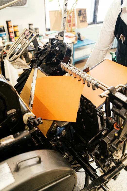 a man working on a machine in a factory, a silk screen, by Jessie Algie, unsplash, private press, black and orange, brown paper, rounded corners, studio bind