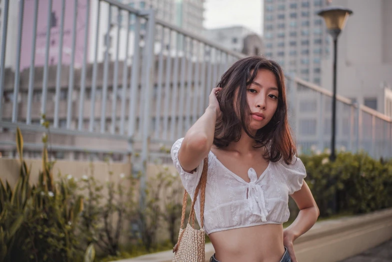 a woman standing on a sidewalk holding a purse, inspired by Tan Ting-pho, pexels contest winner, wearing a crop top, set on singaporean aesthetic, 🤤 girl portrait, white halter top