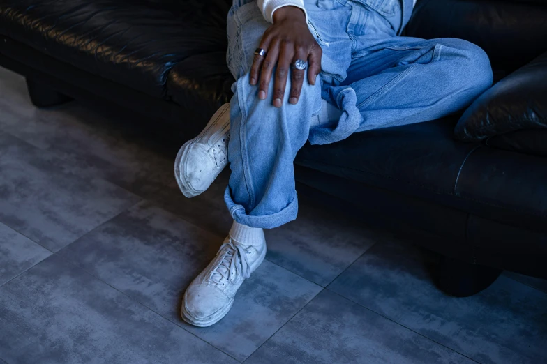 a man sitting on top of a black couch, inspired by Elsa Bleda, trending on pexels, hyperrealism, wearing white sneakers, baggy jeans, riyahd cassiem, androgynous person