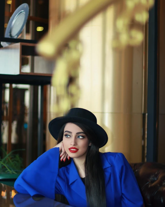 a woman sitting at a table with a hat on, by Julia Pishtar, pexels contest winner, pop art, wearing blue jacket, beautiful iranian woman, 15081959 21121991 01012000 4k, wearing black overcoat