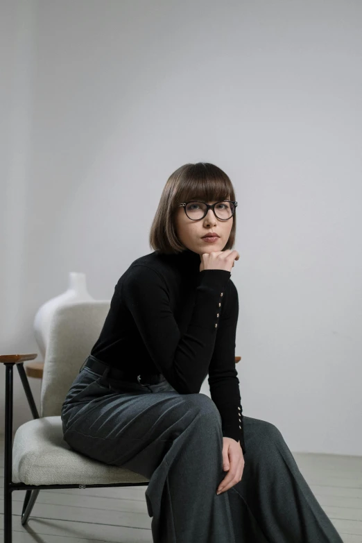 a woman sitting on a chair in a room, a character portrait, inspired by Kim Tschang Yeul, trending on unsplash, in square-rimmed glasses, short brown hair with bangs, style of maciej kuciara, wearing a black sweater