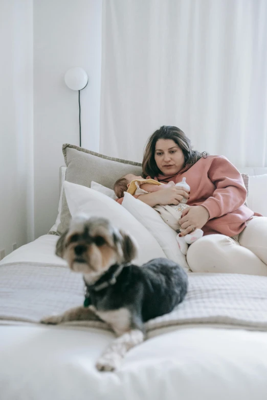 a woman sitting on top of a bed next to a dog, with a kid, maternity feeling, milk, profile image