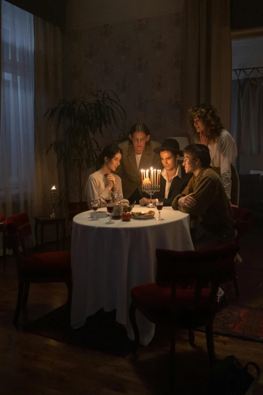 a group of people sitting around a table with a lit candle, by Adam Marczyński, russian cinema, hammershøi, multiple stories, single light