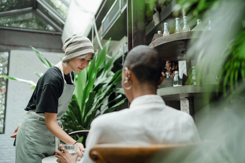 a woman standing next to a woman sitting at a table, by Lee Loughridge, pexels contest winner, lush botany, starbucks aprons and visors, avatar image, its bowl overflowing with plants