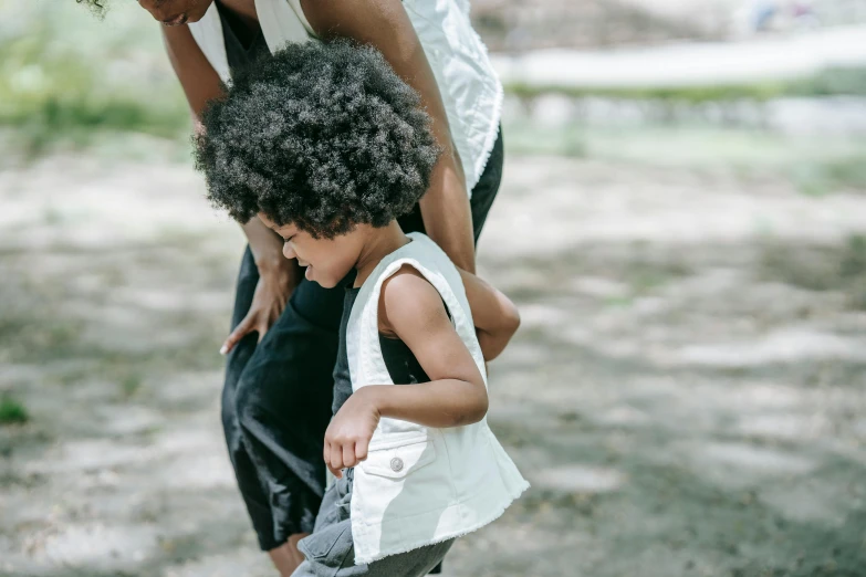 a woman and a child playing with a frisbee, by Nina Hamnett, pexels contest winner, afro hair, head down, ivory and ebony, walking at the garden