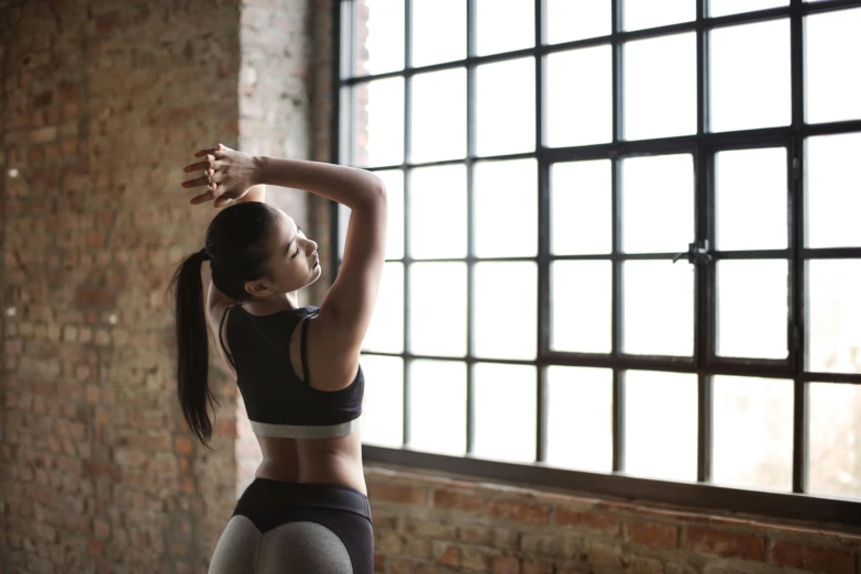 a woman stretching her arms in front of a window, trending on pexels, arabesque, dim dingy gym, shapely derriere, sydney hanson, profile image