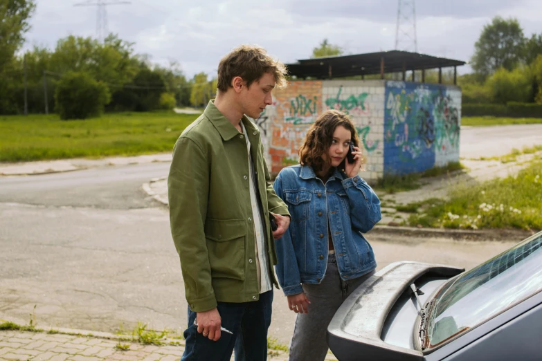 a man and a woman standing next to a car, by Adam Marczyński, happening, still image from tv series, checking her phone, cynthwave, berberic clothes