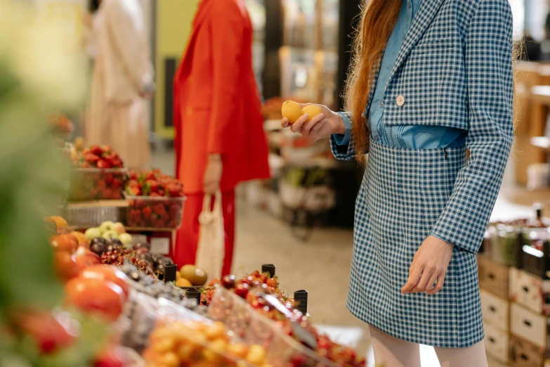 a woman standing in front of a fruit stand, pexels contest winner, short skirt and a long jacket, inspect in inventory image, wearing a light blue suit, girl wears a red dress