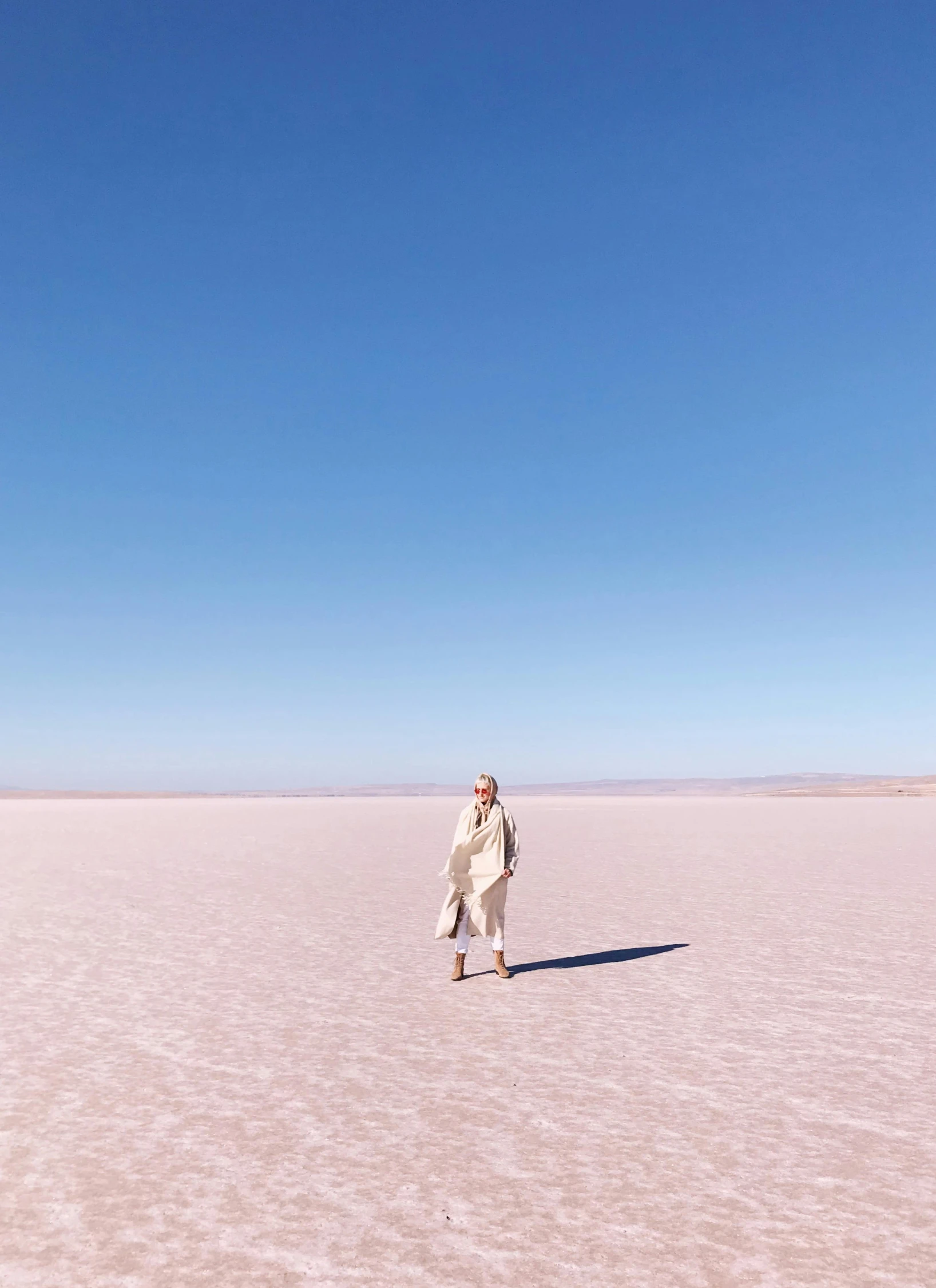 a man standing in the middle of a desert, inspired by Scarlett Hooft Graafland, trending on unsplash, land art, wearing a light - pink suit, dressed in an old white coat, patagonian, standing on the water ground