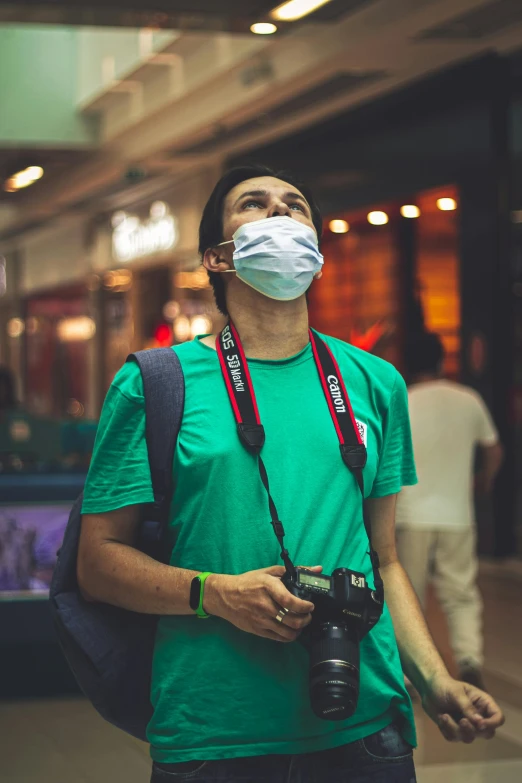 a man wearing a face mask while holding a camera, pexels contest winner, in a mall, wearing green, sickness, avatar image