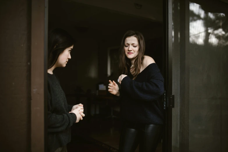 a woman standing next to another woman in a doorway, pexels contest winner, happening, dark people discussing, at home, spring season, solemn gesture