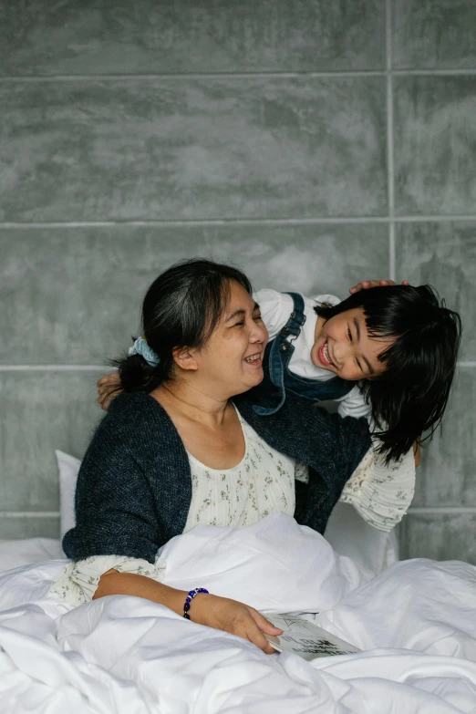 a couple of women sitting on top of a bed, inspired by Ruth Jên, pexels contest winner, incoherents, with a kid, earing a shirt laughing, gif, asian woman