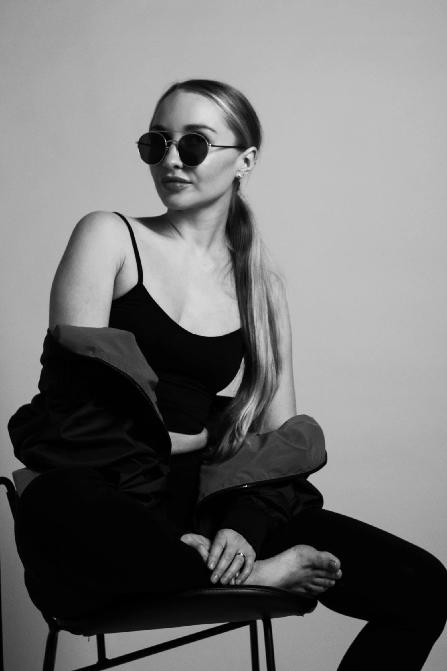 a black and white photo of a woman sitting on a chair, a black and white photo, inspired by Ion Andreescu, trending on pexels, portrait of kim petras, black sunglasses, wearing a track suit, shot in the photo studio