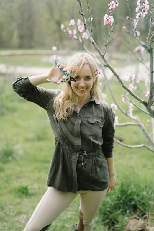 a woman standing next to a tree in a field, holding magical kitchen knives, evanna lynch, in bloom greenhouse, anna nikonova aka newmilky