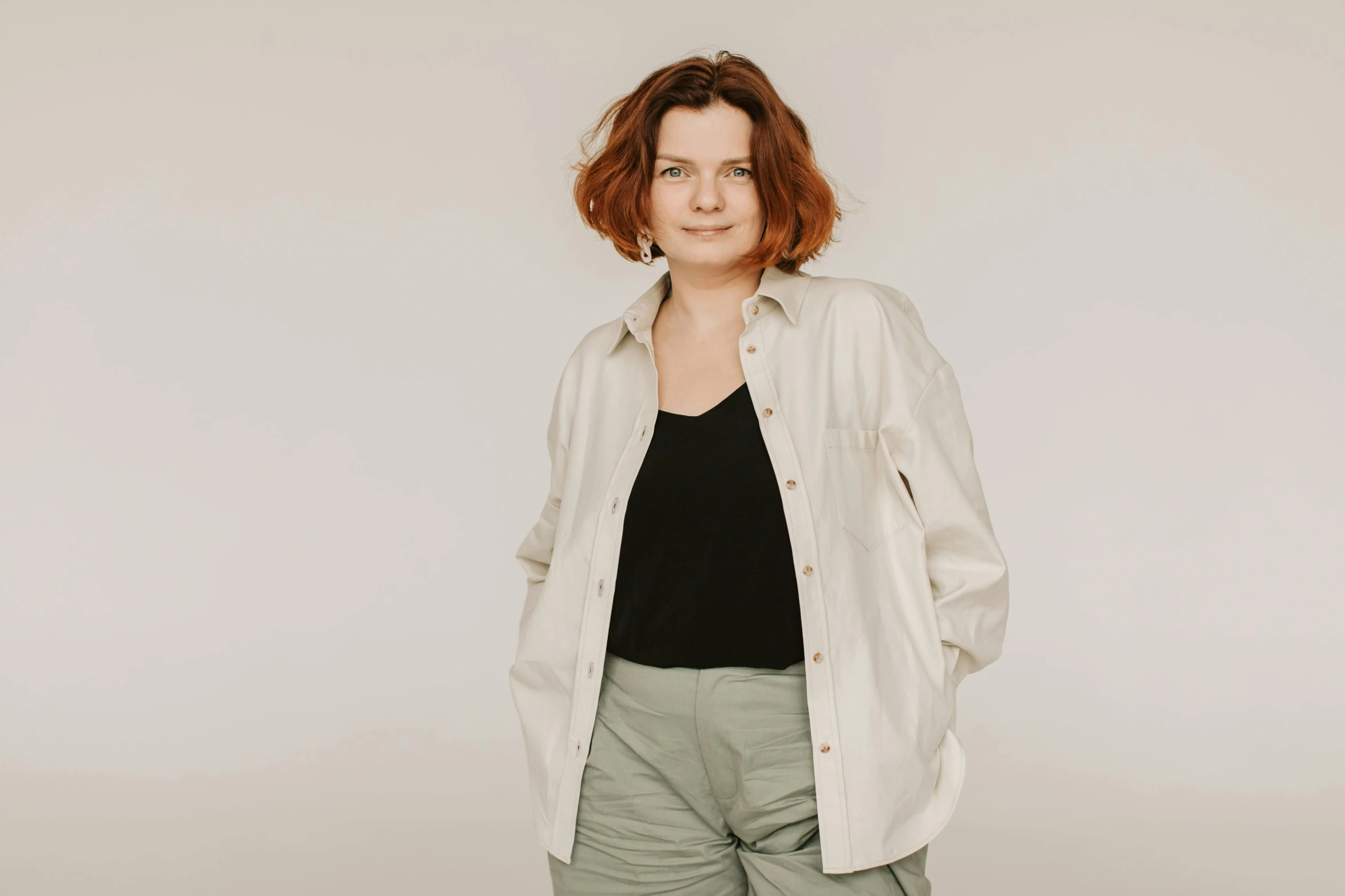 a woman standing in front of a white wall, by Emma Andijewska, trending on pexels, button - up shirt, plus-sized, ivory and copper, nikolay georgiev