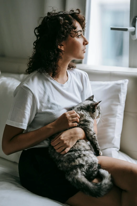 a woman sitting on a bed holding a cat, trending on pexels, sitting on the couch, looking off into the distance, hugging each other, full product shot