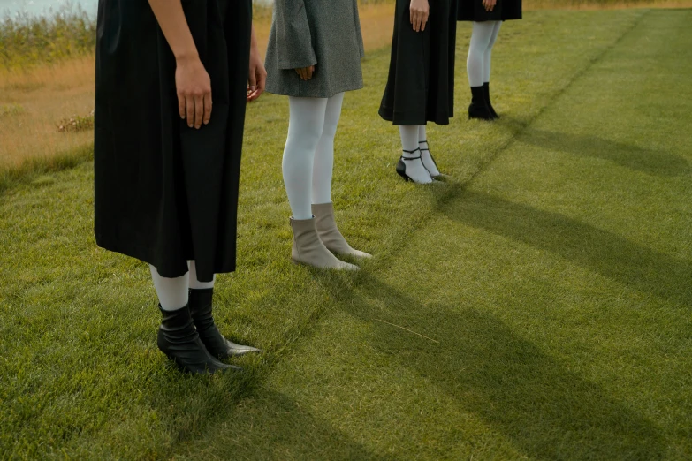 a group of people standing on top of a lush green field, inspired by Vanessa Beecroft, pexels contest winner, aestheticism, white blouse and gothic boots, standing in class, fashion show photo, grey clothes