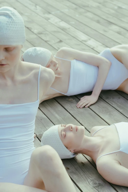 a group of women laying on top of a wooden floor, inspired by Vanessa Beecroft, unsplash, aestheticism, wearing a white bathing cap, albino white pale skin, three head one body, spa