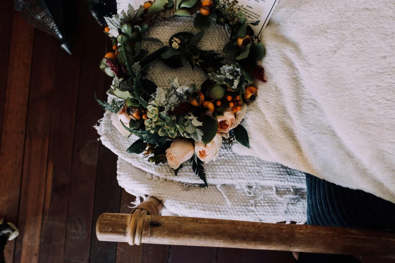 a wreath sitting on top of a bed next to a pillow, a still life, by Carey Morris, pexels contest winner, holding a wooden staff, manuka, made of flowers and berries, autumn