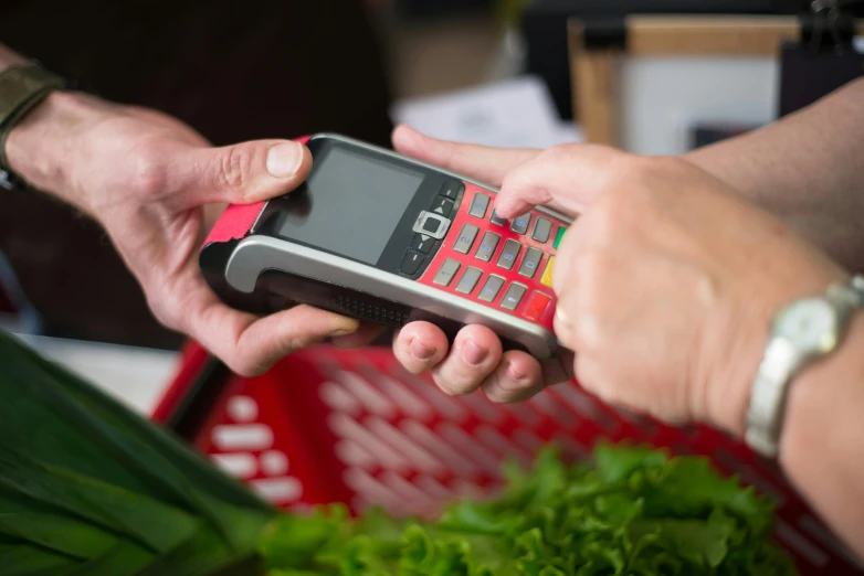 a close up of a person holding a cell phone, at checkout, vibrant red and green colours, market setting, psion