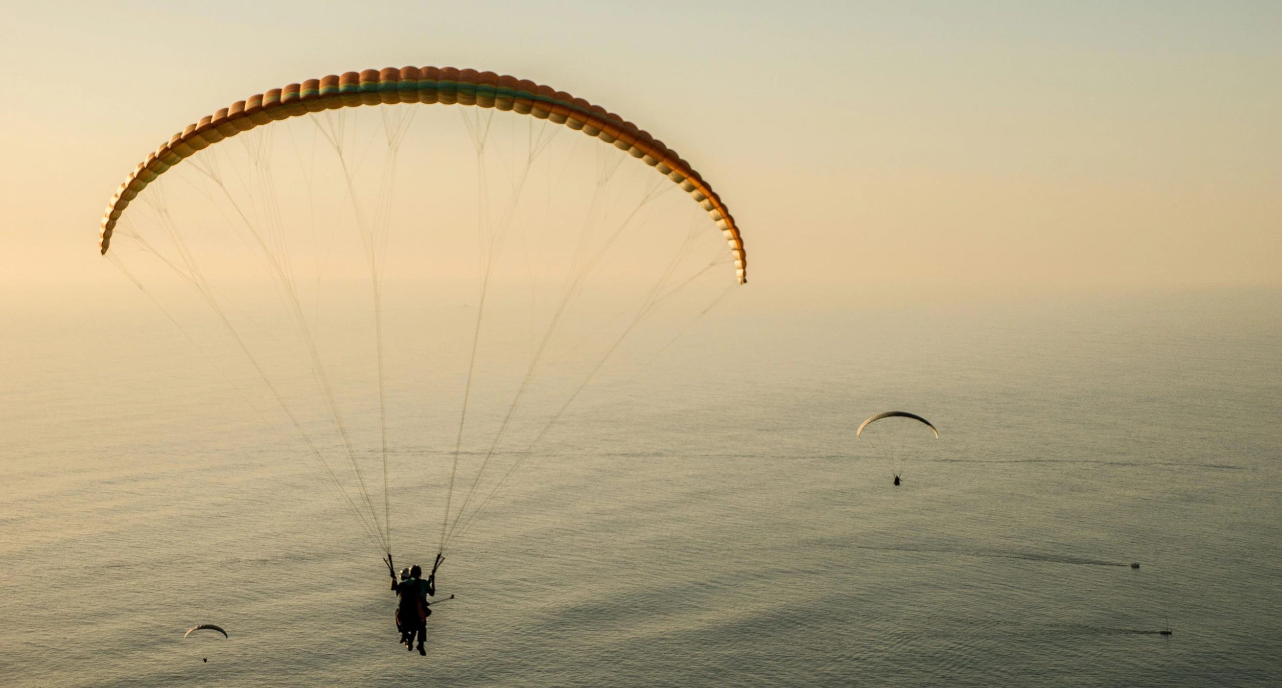 a person flying a parachute over a body of water, overlooking the ocean, greg rutkowski and craig mullins, at the golden hour, male and female