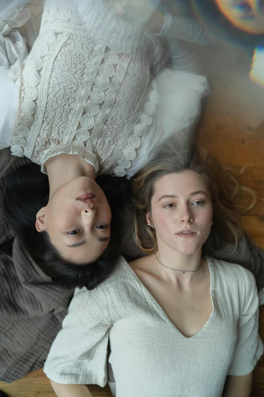 a couple of women laying on top of a wooden floor, inspired by Wang Duo, unsplash, photorealism, pale complexion, loving stare, perfectly lit. movie still, college