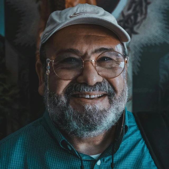 a close up of a person wearing glasses and a hat, a character portrait, inspired by Arturo Rivera, pexels contest winner, arab man light beard, smiling for the camera, portrait of real life totoro, icon