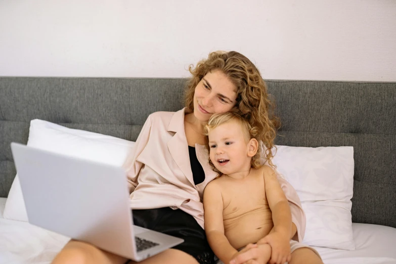 a woman and child sitting on a bed with a laptop, by Carey Morris, pexels, avatar image, toddler, 1 5 0 4, brown