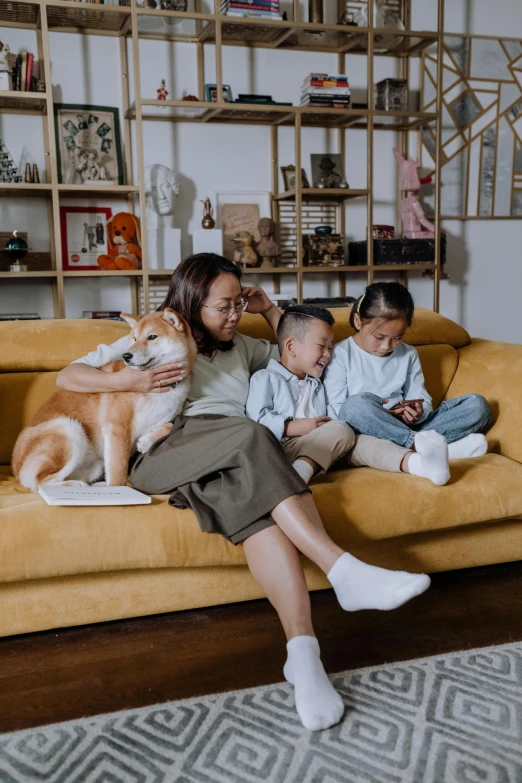 a woman sitting on a couch with two children and a dog, by Basuki Abdullah, pexels contest winner, set on singaporean aesthetic, with cats on her side, with a long, hunting