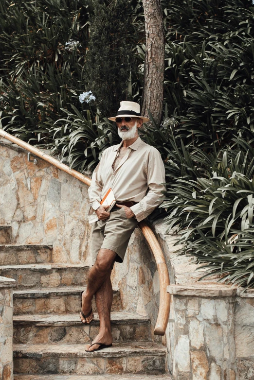 a man standing at the top of a set of stairs, a portrait, inspired by Tomàs Barceló, pexels contest winner, tan shorts, old gigachad with grey beard, tropical style, caracter with brown hat