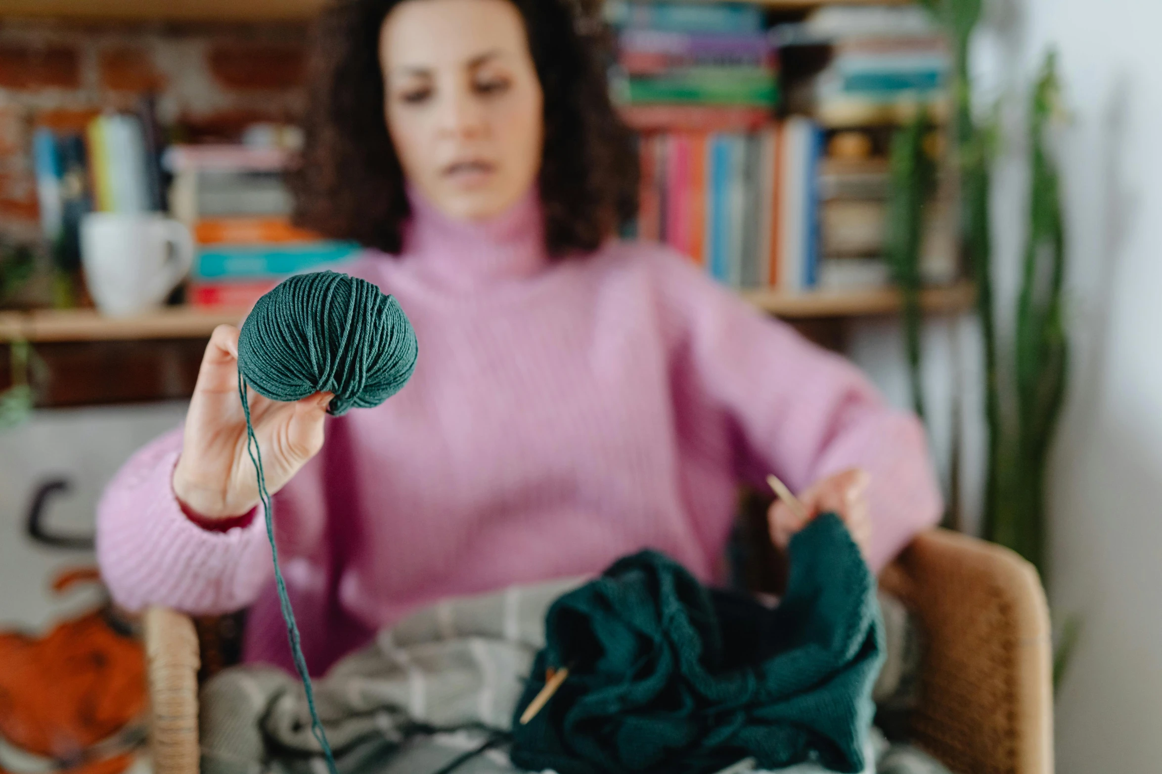 a woman sitting in a chair holding a ball of yarn, trending on pexels, arts and crafts movement, wearing a green sweater, mid - action, unblur, with teal clothes