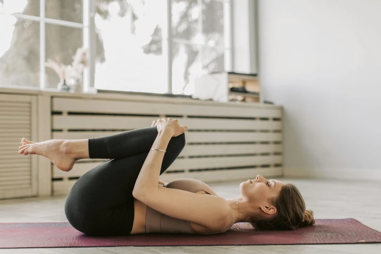 a woman laying on her stomach on a yoga mat, by Rachel Reckitt, trending on pexels, arabesque, hugging her knees, manuka, local gym, back arched