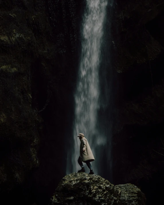 a person standing in front of a waterfall, on a dark background, instagram post, she is wearing a wet coat, ansel ]