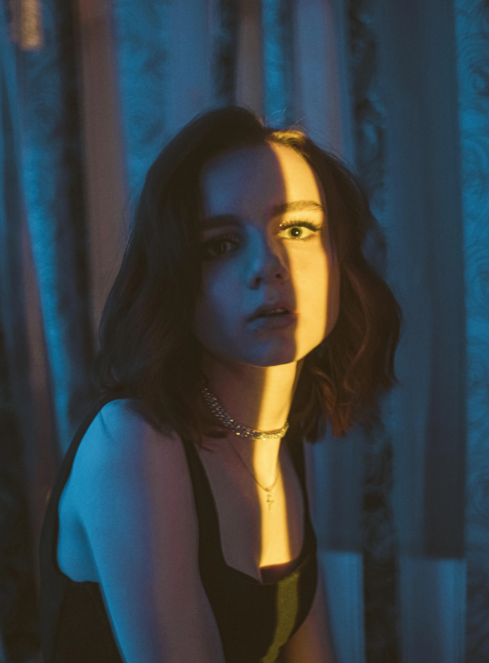 a woman sitting on top of a bed next to a window, an album cover, inspired by Elsa Bleda, unsplash, police lights shine on her face, sadie sink, gif, looking serious